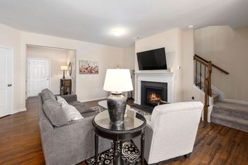 Cozy living room with gray sofa, white chairs, fireplace, TV, and staircase