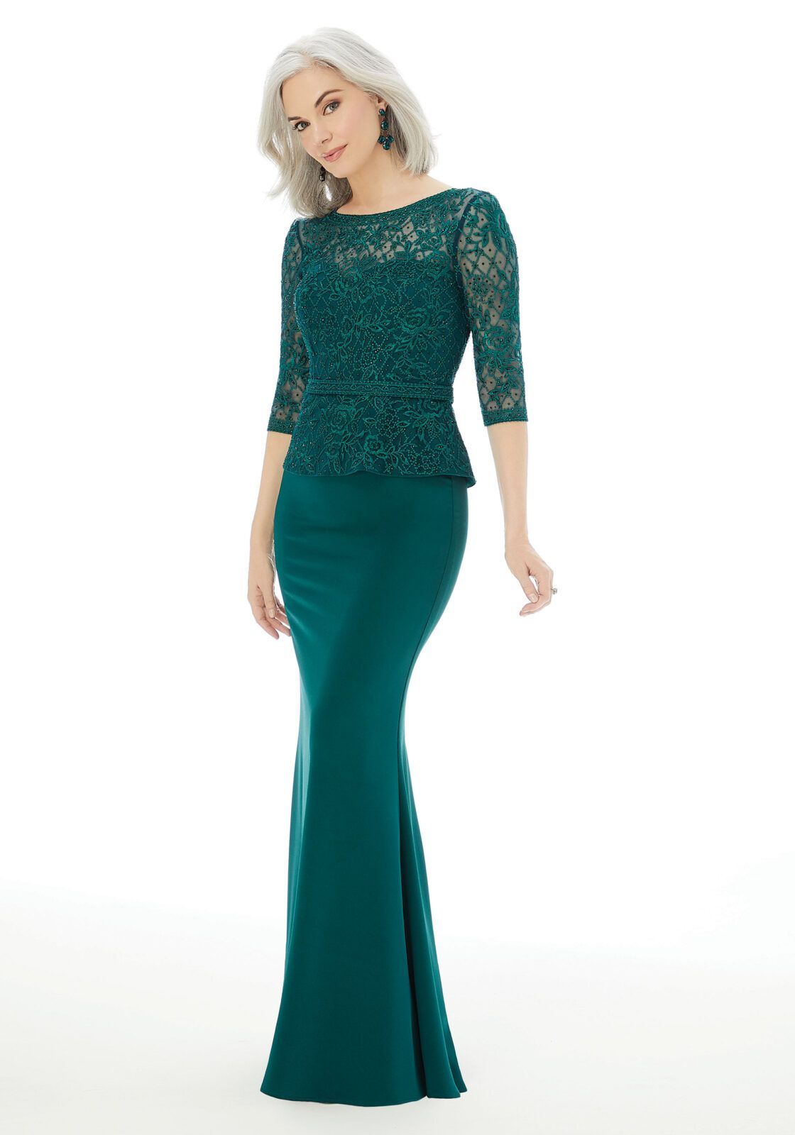 Una modella indossa un abito lungo fino ai piedi, a maniche lunghe, di colore verde scuro, con corpetto in pizzo, su uno sfondo bianco uniforme.