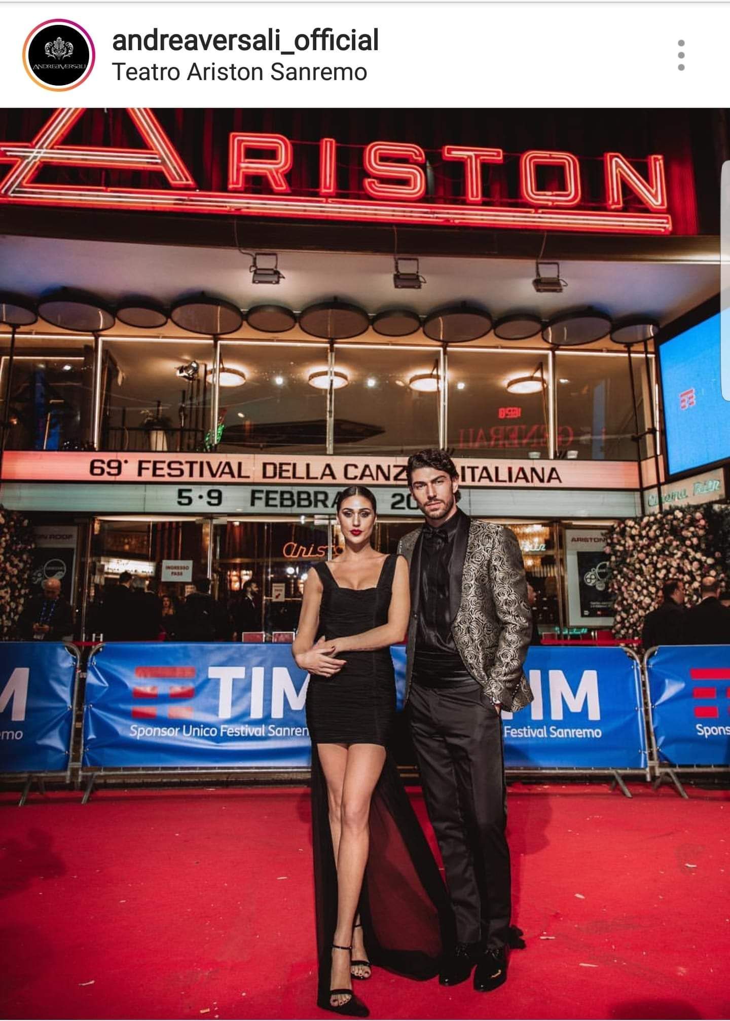 Una coppia posa su un tappeto rosso davanti al Teatro Ariston illuminato al Festival di Sanremo.