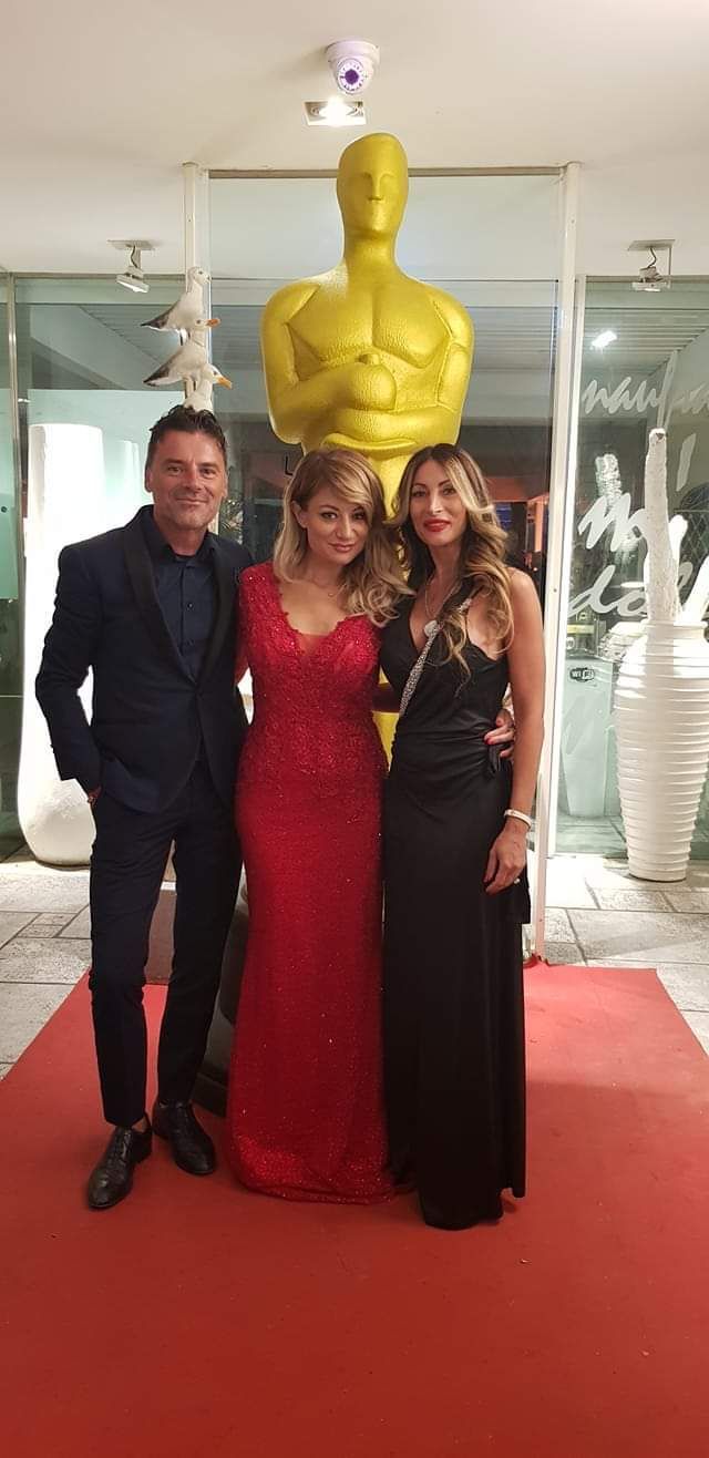 Tre persone sono in piedi su un tappeto rosso di fronte a una grande statuetta dorata dell'Oscar.