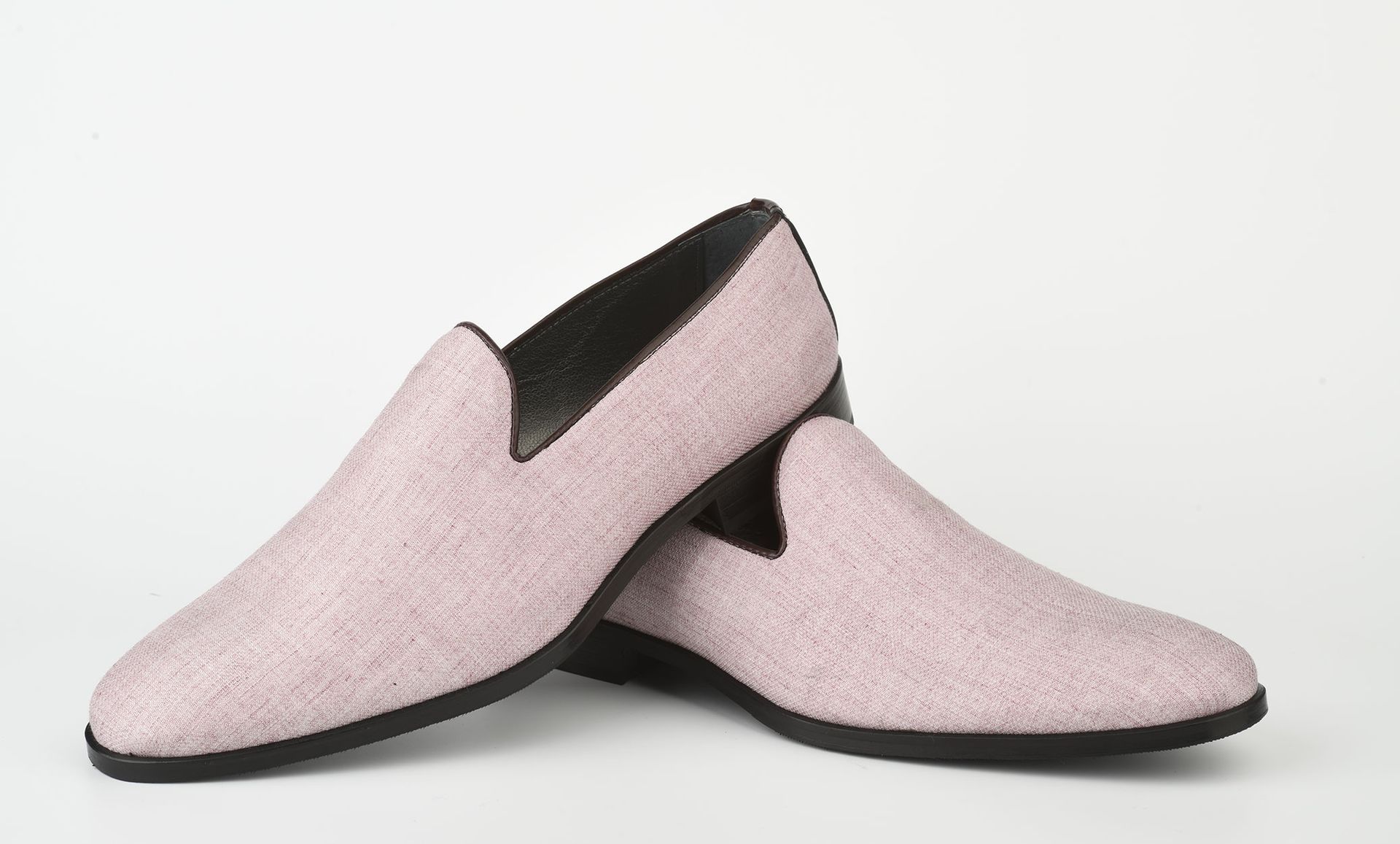 Un paio di mocassini slip-on rosa chiaro con texture e suola scura su sfondo bianco.