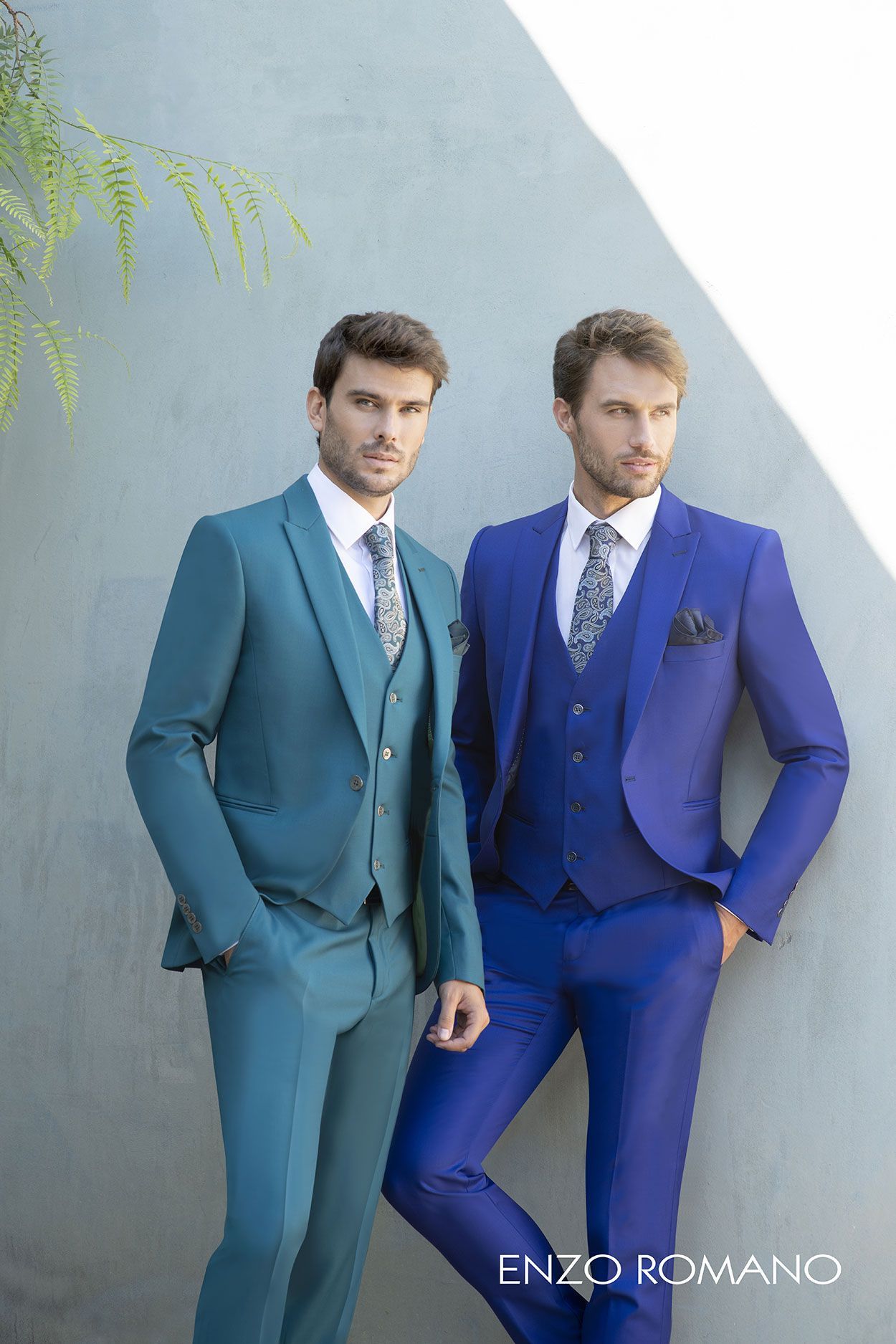 Due uomini sono in piedi fianco a fianco in abiti formali, uno con un abito a tre pezzi color verde acqua e l'altro con un abito a tre pezzi blu reale.