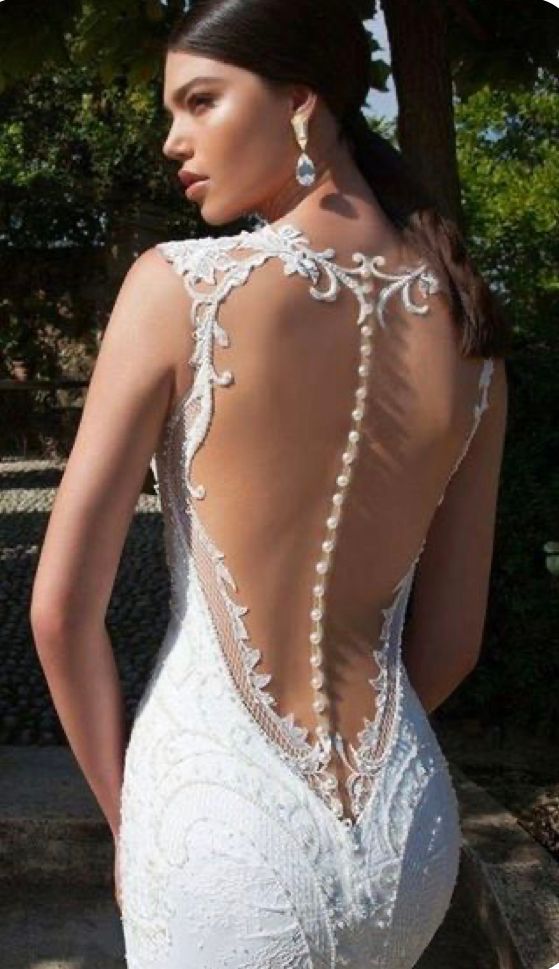 Una modella indossa un abito da sposa bianco in pizzo, lungo fino ai piedi, con schiena scoperta e una lunga fila di bottoni.