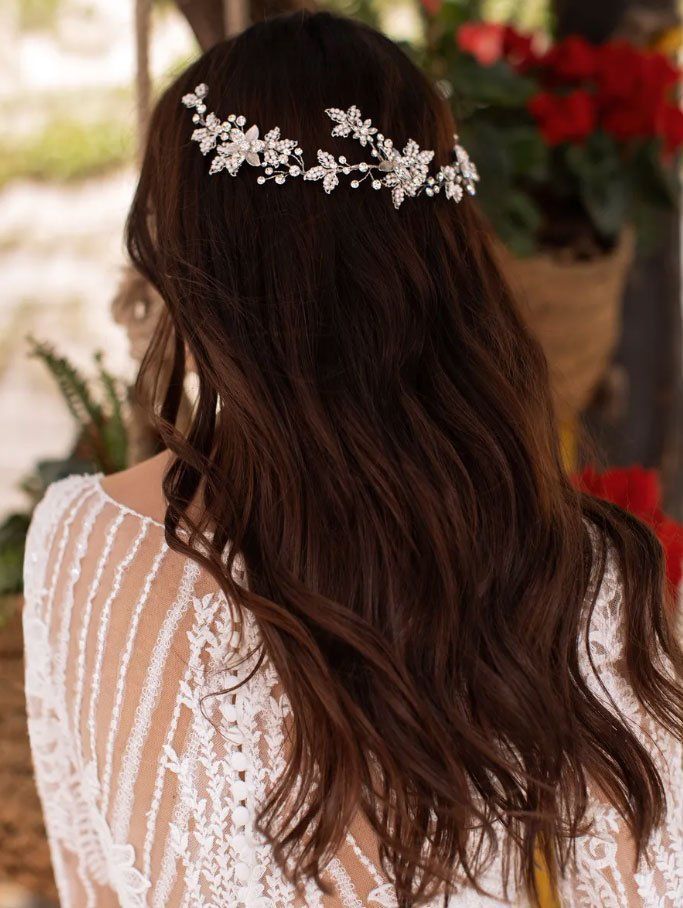 Una persona con lunghi capelli scuri e ondulati, che indossa un fermaglio decorativo argentato a forma di fiore, vista di spalle.