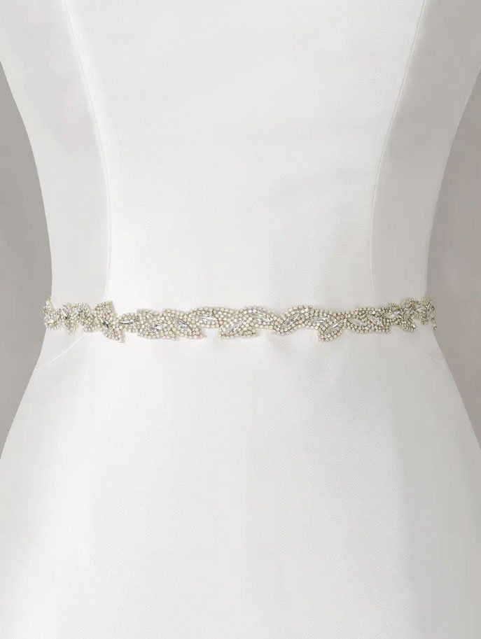 Una sottile cintura da sposa argentata, impreziosita da cristalli, indossata intorno alla vita di un semplice abito bianco.