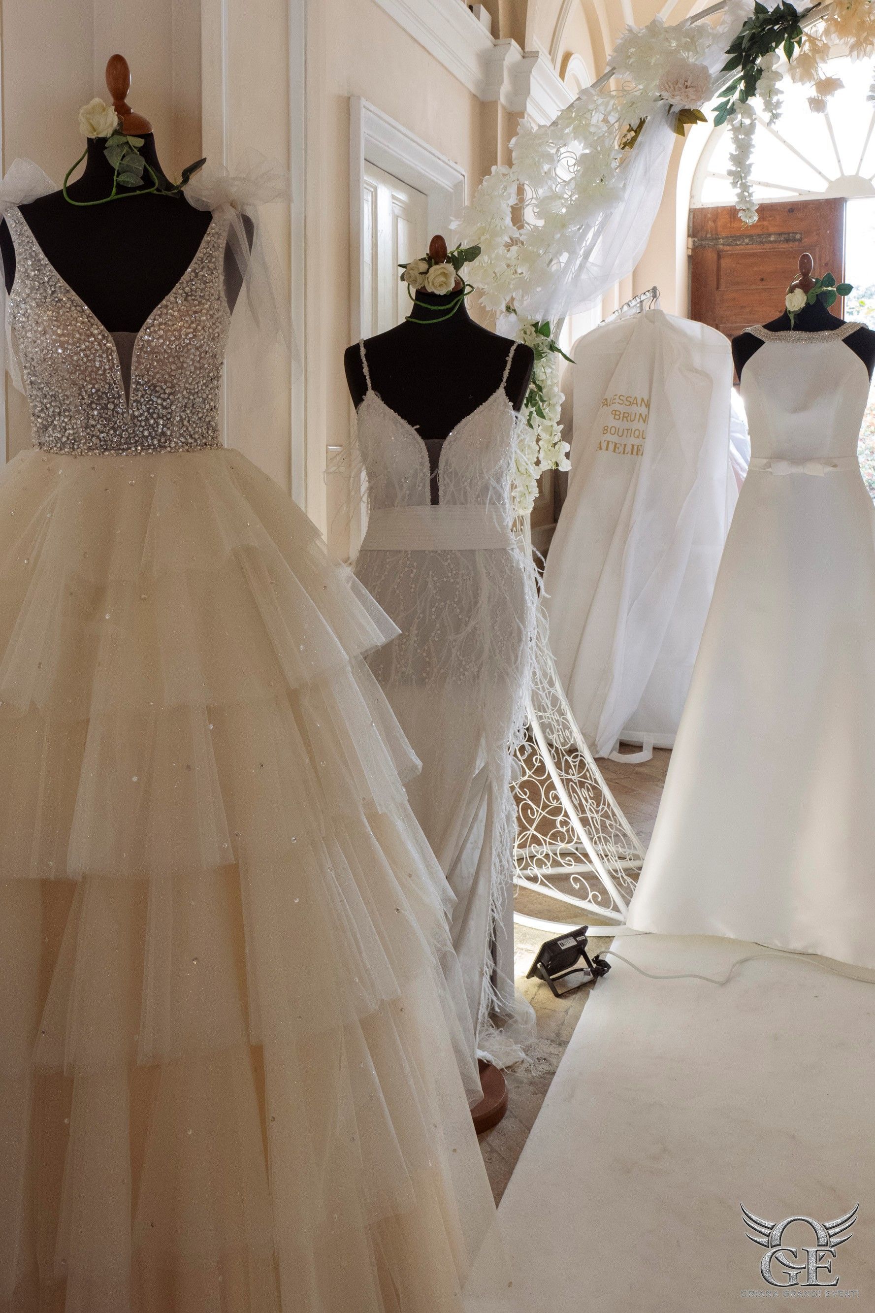Tre abiti da sposa esposti su manichini in un negozio di abiti da sposa, con modelli a strati, in pizzo e in raso.