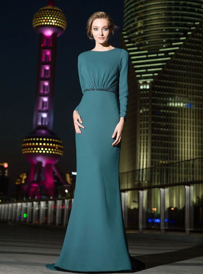 Di notte, una persona posa indossando un lungo abito a maniche lunghe color verde acqua, con la Torre della Perla Orientale illuminata sullo sfondo.
