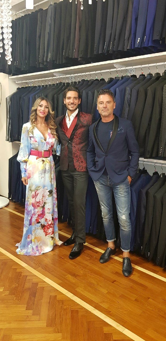 In un negozio di abbigliamento pieno di abiti eleganti, tre persone sorridono verso la telecamera.