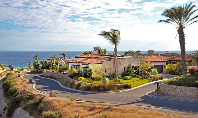 A large house is sitting on top of a hill next to the ocean.