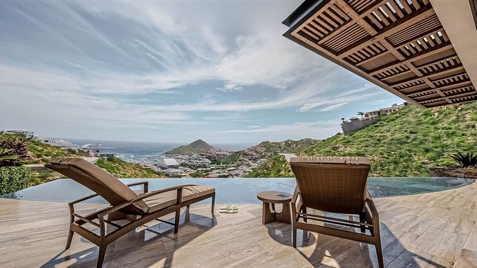 Two lounge chairs are sitting next to a swimming pool with a view of the ocean.
