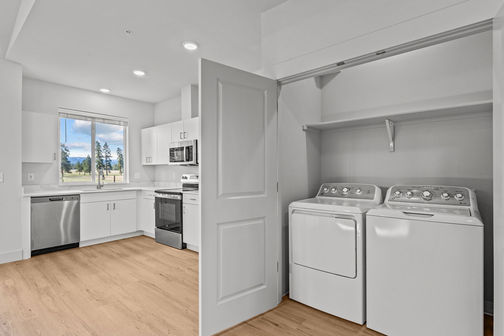 A hallway with white cabinets and wooden floors leading to a door.
