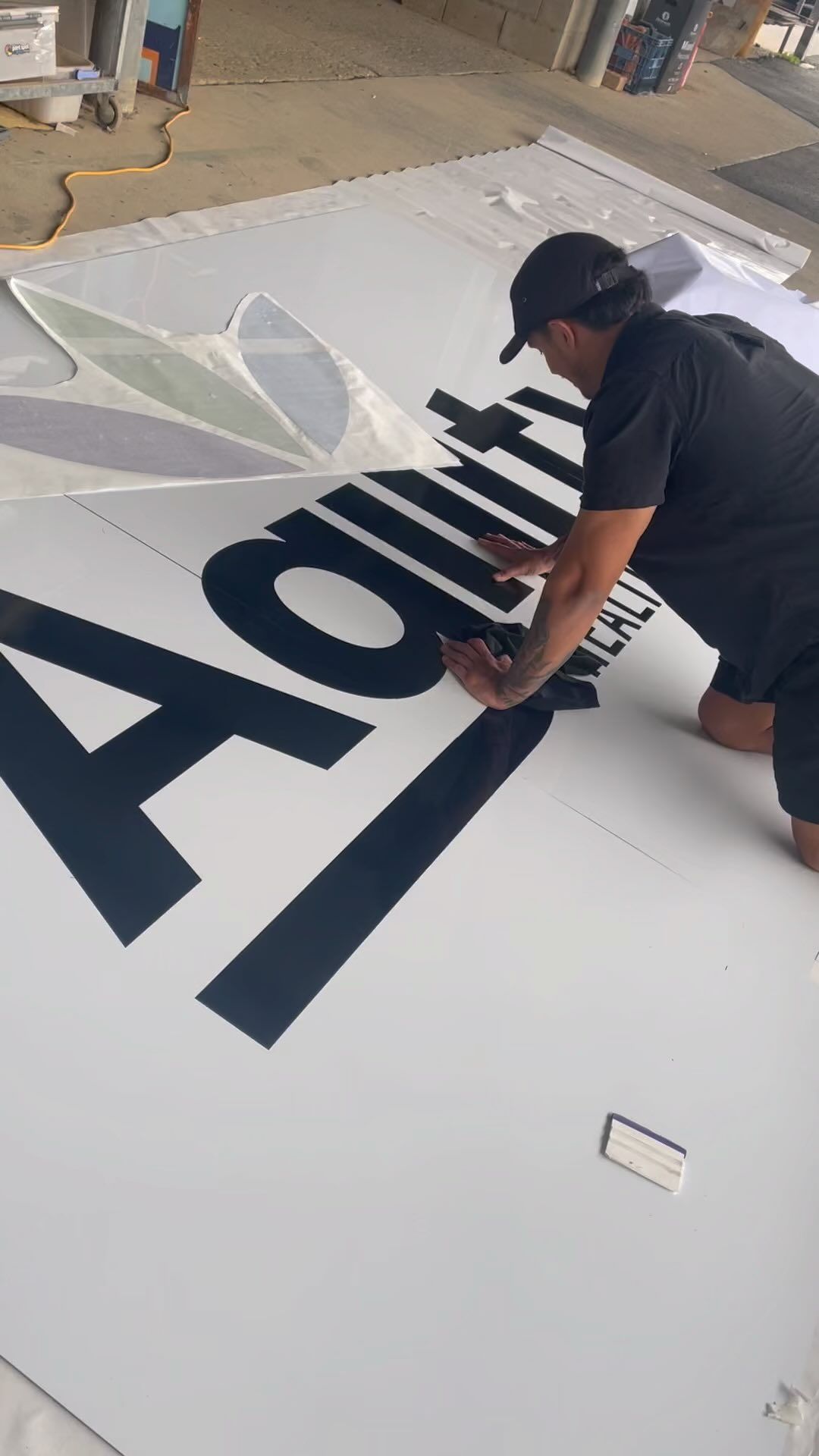 A Man is Kneeling on the Ground Painting a Large Sign — Print Spot Group in Byron Bay, NSW