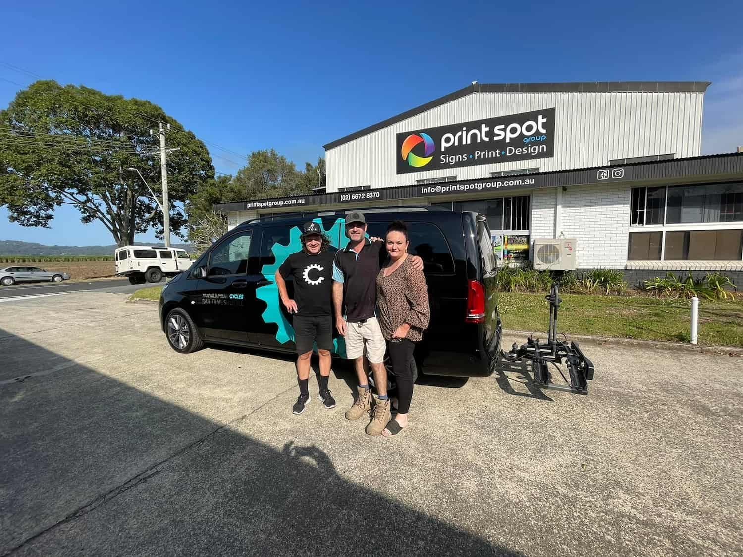 Three People Stand in Front of a Black Van With a Print Spot Logo and Building — Print Spot Group in South Murwillumbah, NSW