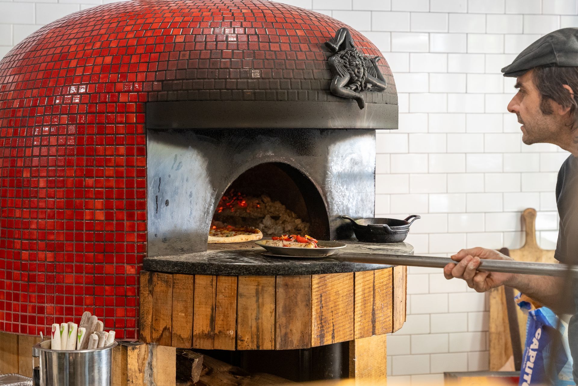 A man is putting a pizza into a pizza oven.