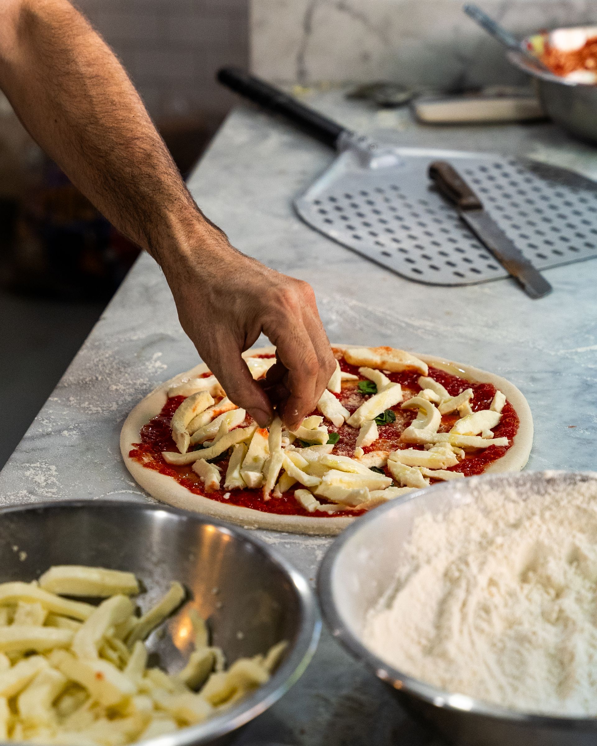 A person is putting cheese on a pizza on a table.