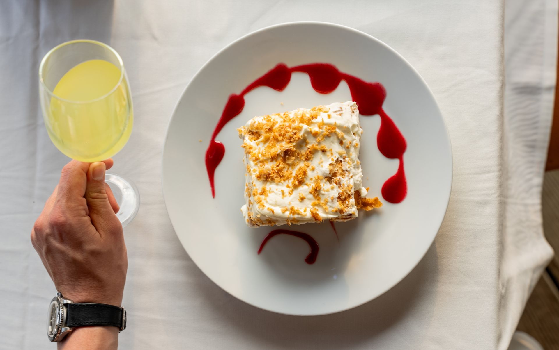 A person is holding a glass of wine next to a plate of food.