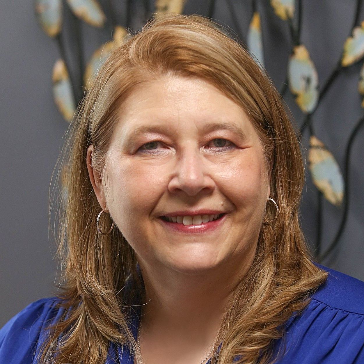 A woman wearing glasses and a pink shirt is smiling for the camera.
