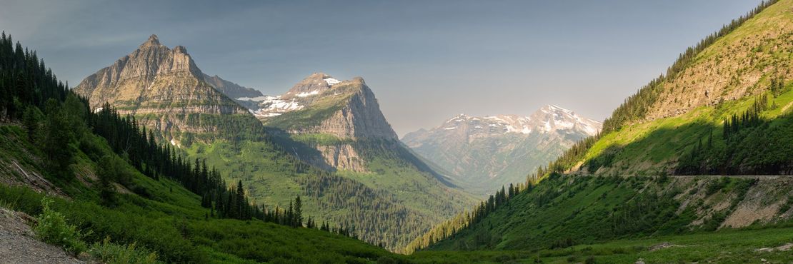 Mountain valley with green forests, rocky peaks, and snowy mountains under a clear sky