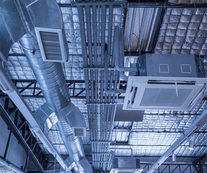 Blue-tinted industrial ceiling with exposed ducts, pipes, vents, and grid lighting.