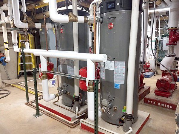 Two water heaters are sitting next to each other in a room with pipes.