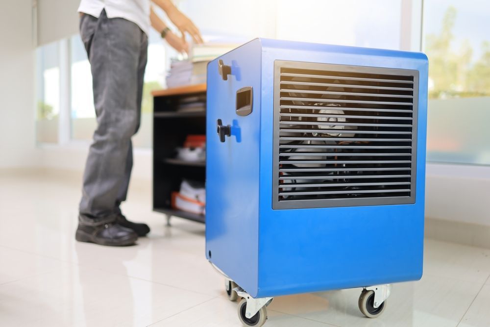 A man is standing next to a blue air cooler on wheels.