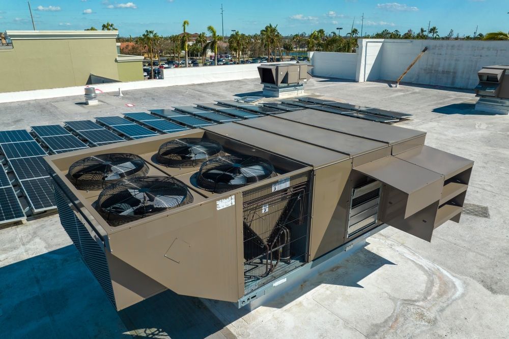 Large rooftop HVAC units beside solar panels on a flat white roof near the sea