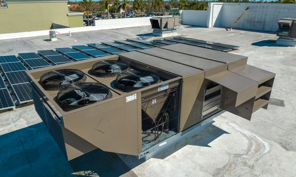 Large rooftop HVAC units and solar panels on a flat white roof under a clear blue sky