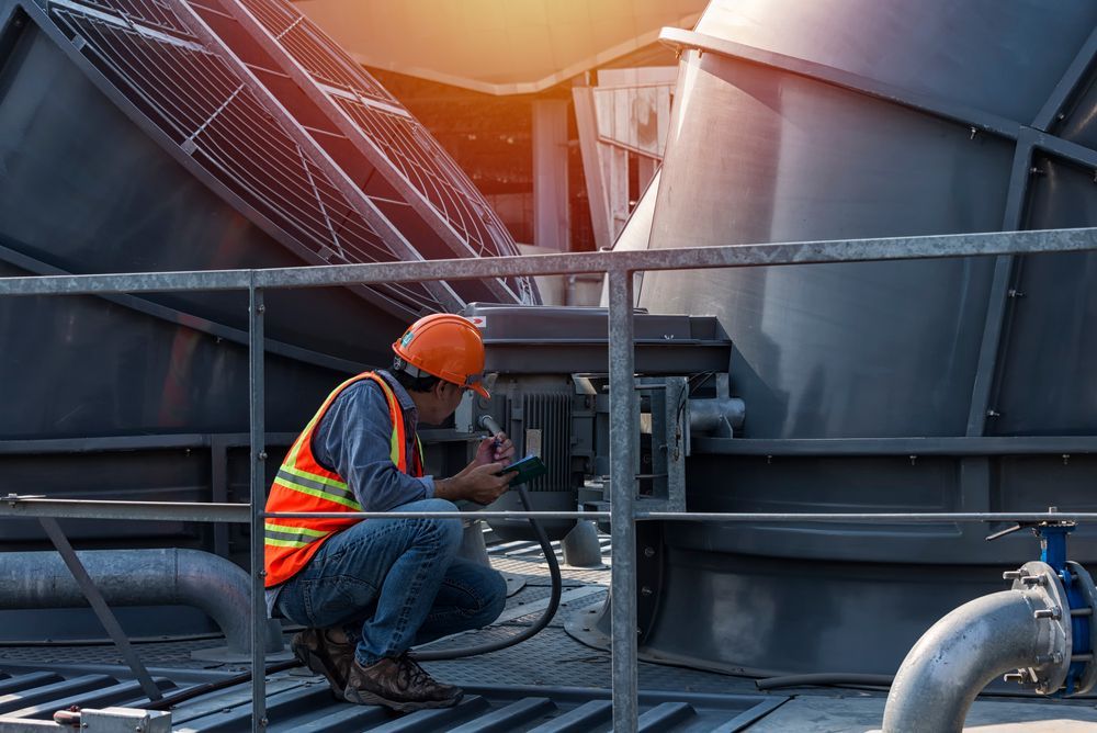 a man in a hard hat is working on a component of an HVAC cooling tower.