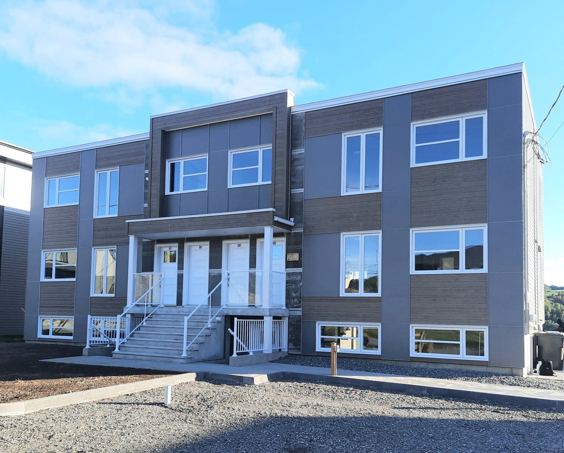 Immeuble d'appartements moderne de deux étages avec extérieur gris et brique, fenêtres et portes blanches.