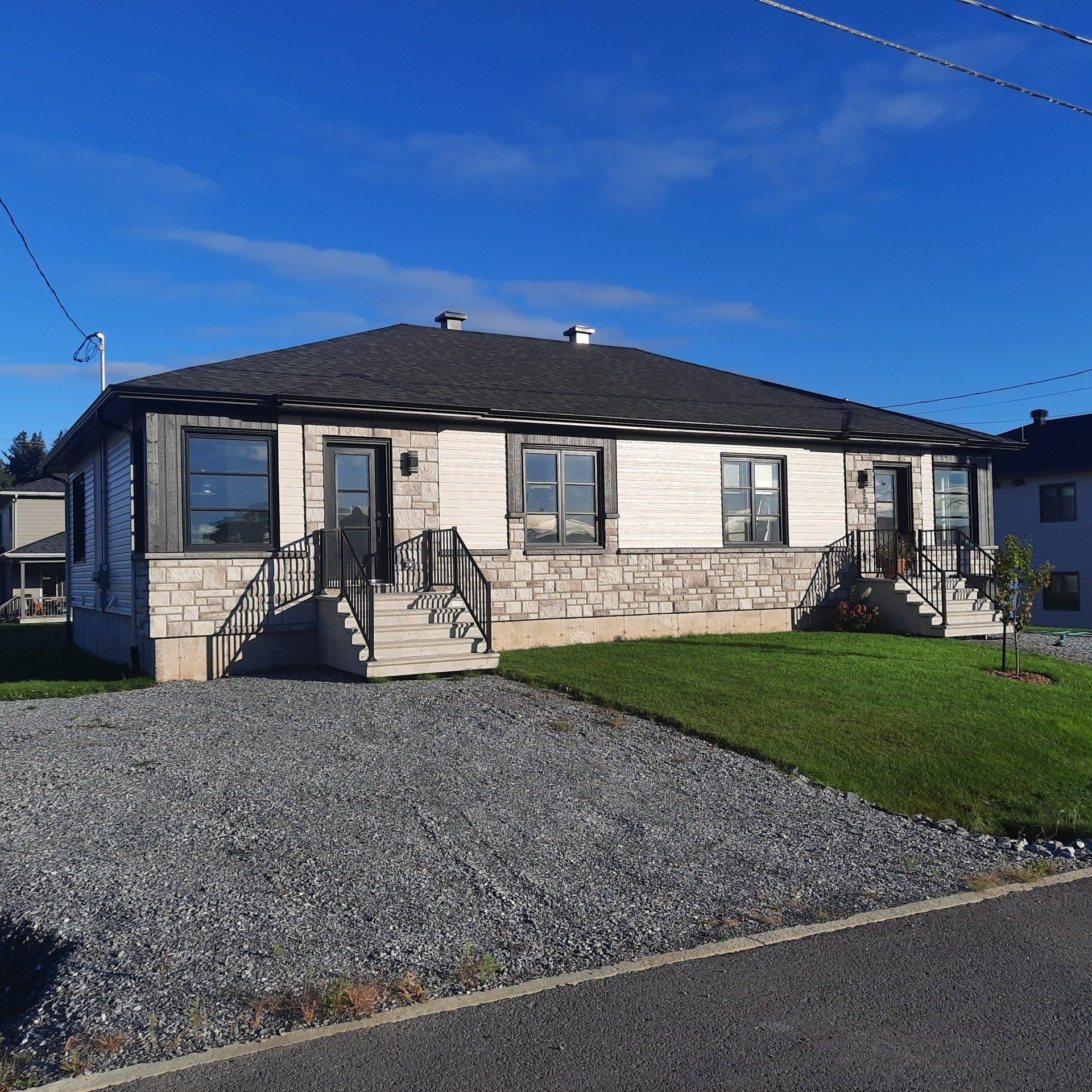 Duplex en pierre sous ciel bleu avec allée en gravier et petite pelouse.