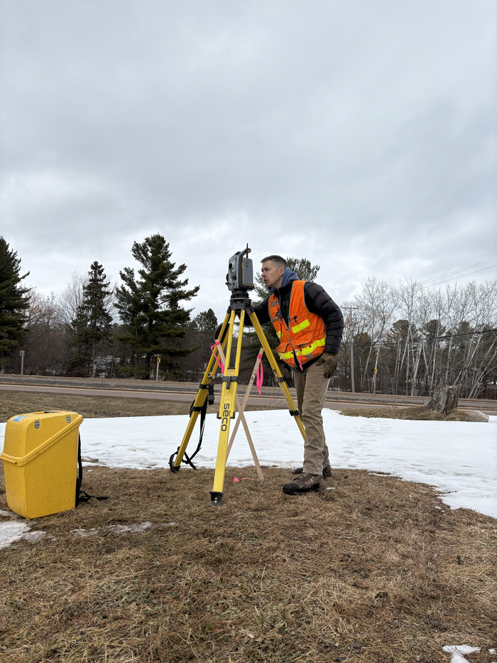 Surveyor in orange safety vest using a tripod-mounted instrument on a snowy field