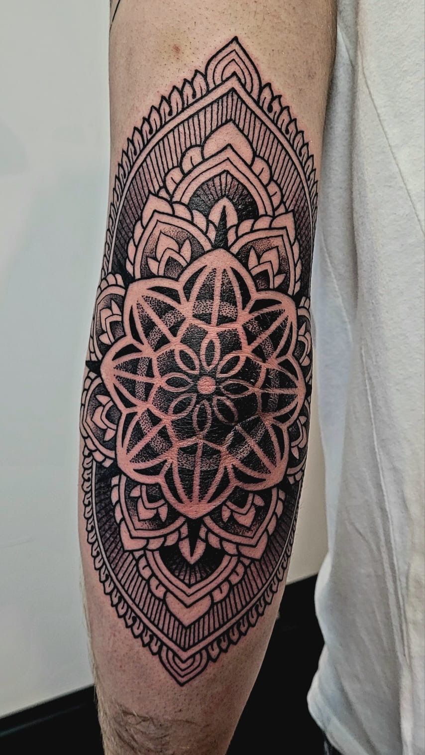A close-up of a person's elbow featuring a large, intricate black-ink mandala tattoo with geometric patterns.