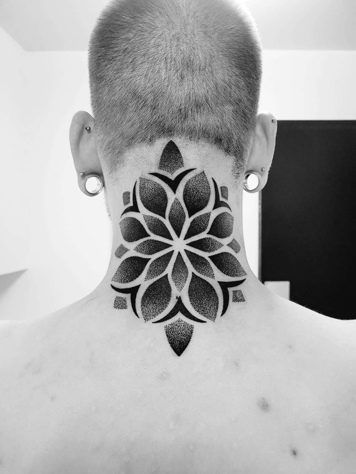 A black and white geometric mandala tattoo on the back of a person's neck.