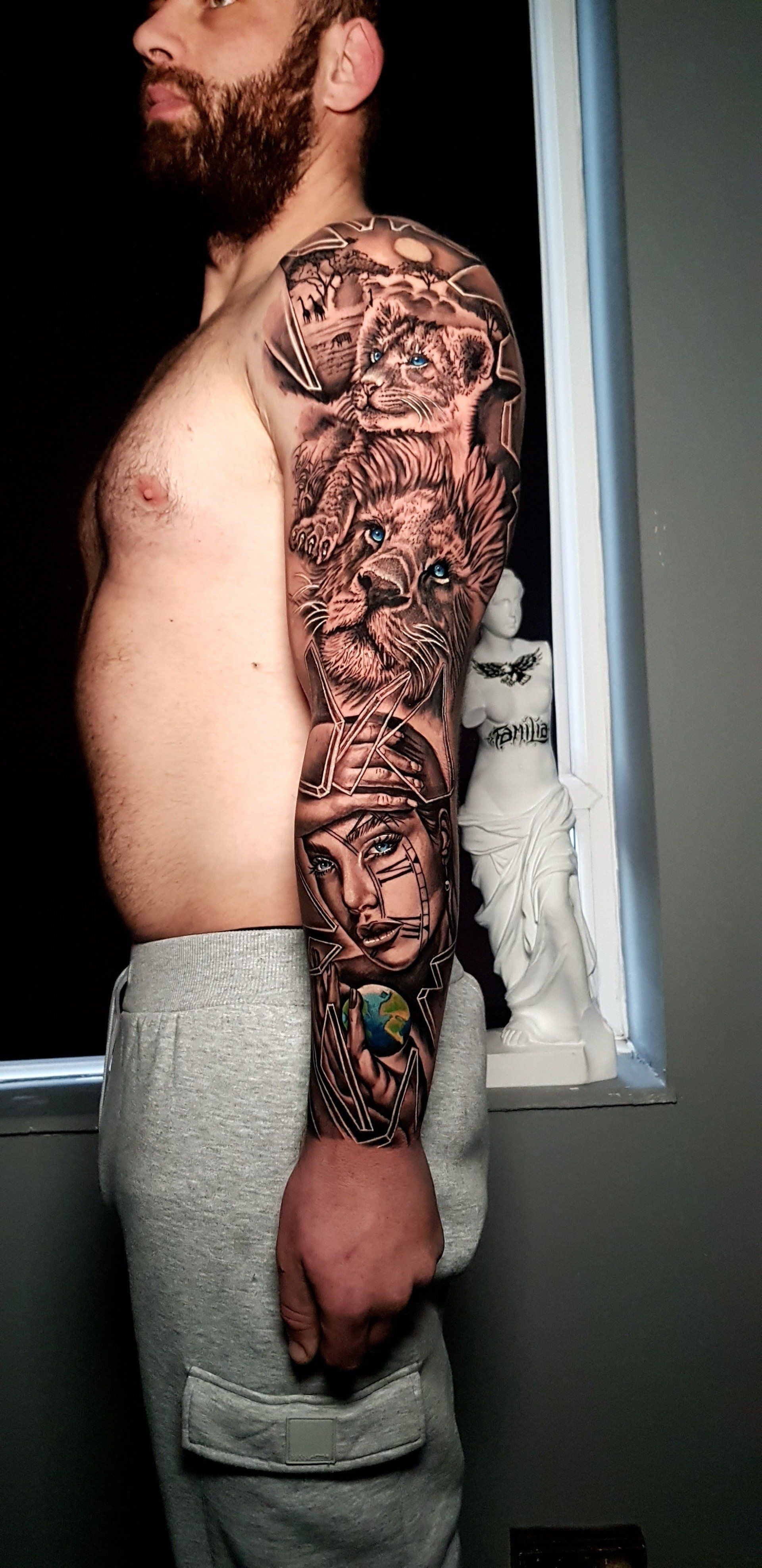 A person stands in profile, displaying a detailed, monochromatic tattoo sleeve covering their entire left arm.