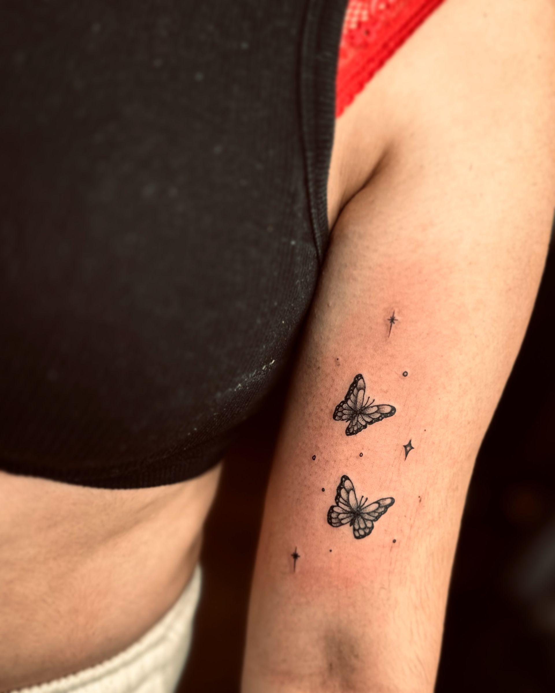 A close-up of a forearm featuring a small tattoo of two butterflies surrounded by delicate, tiny sparkling stars.