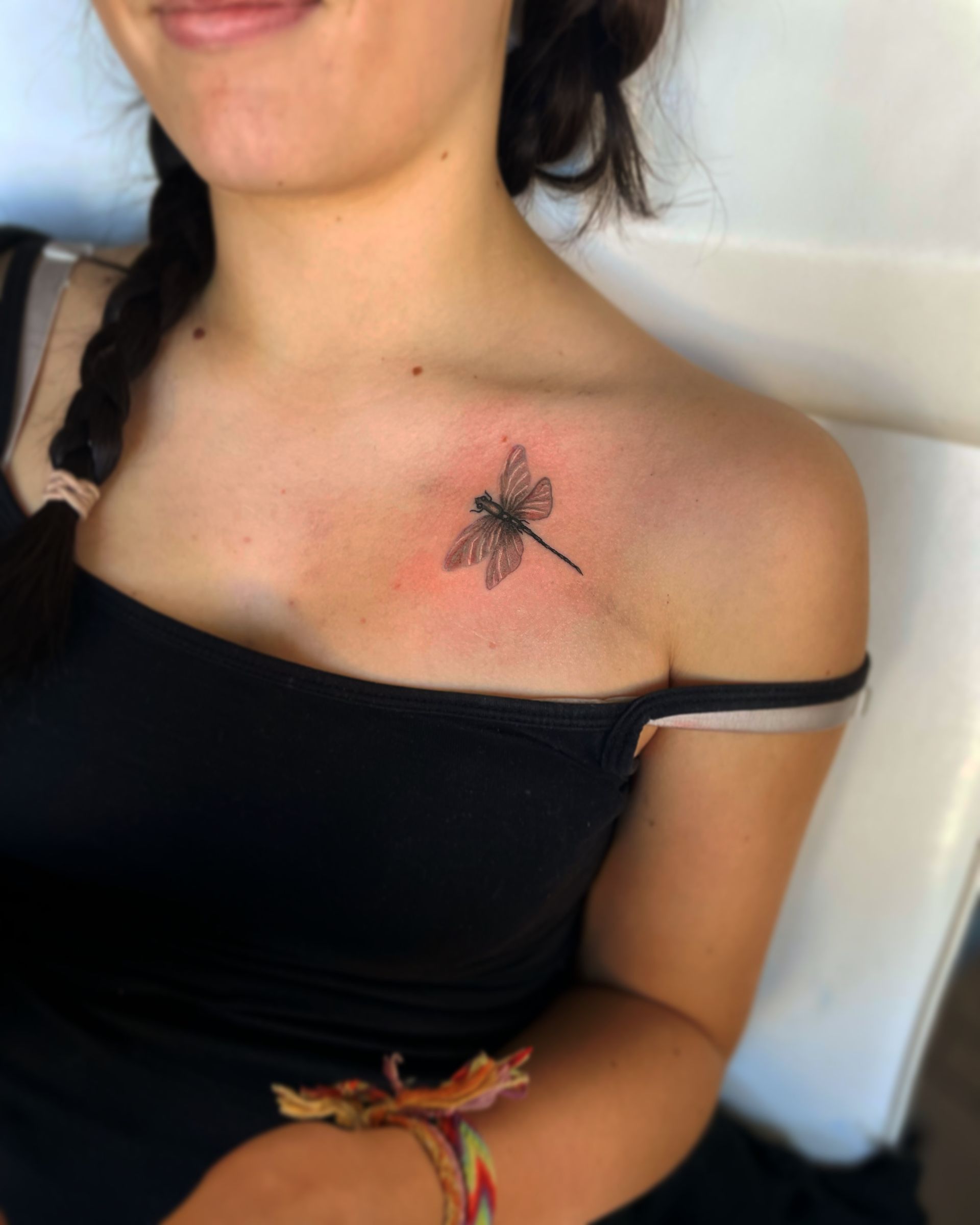 A person with a delicate, detailed black-ink dragonfly tattoo on their upper chest near the collarbone.