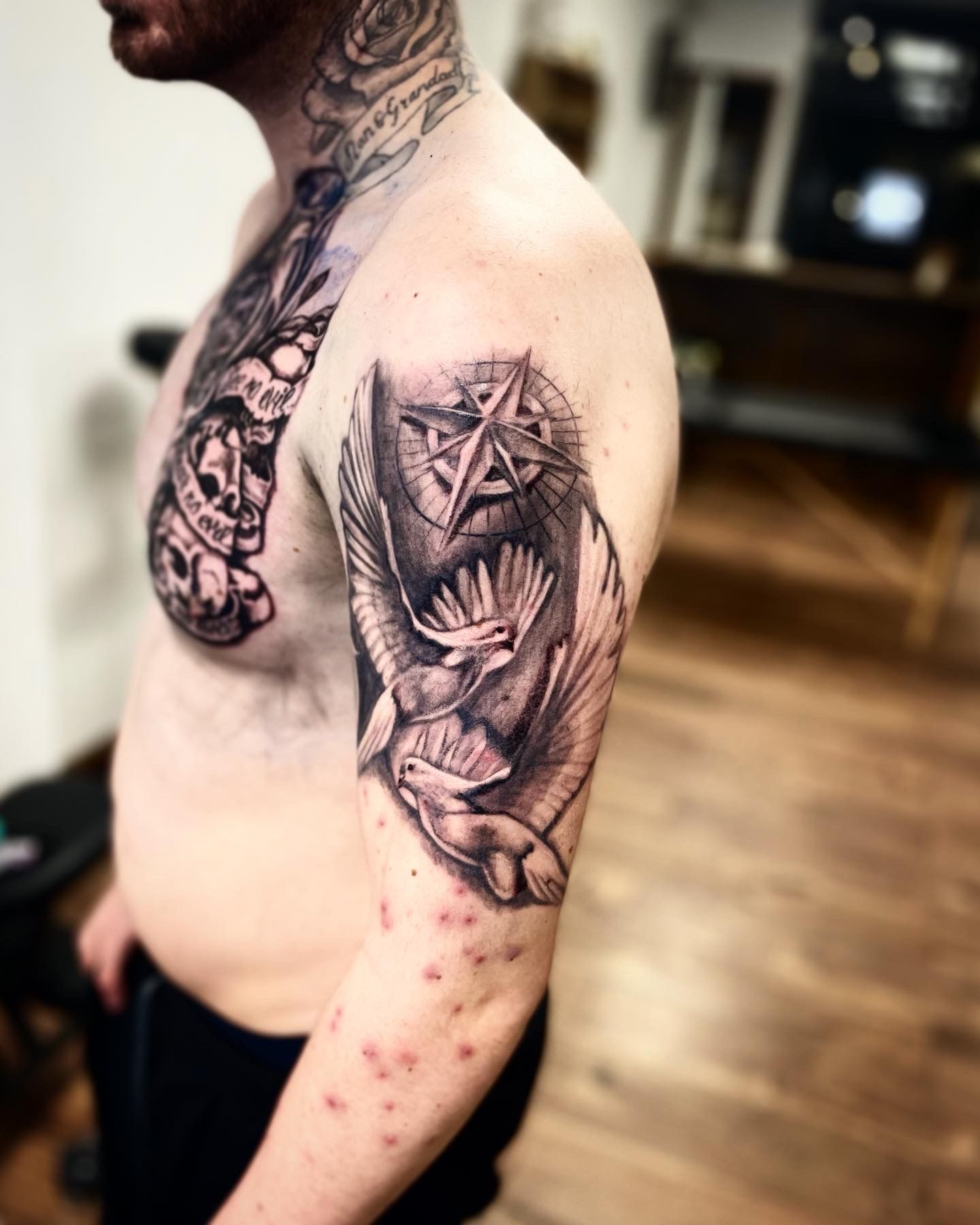 A person showing a new black and gray tattoo on their upper arm featuring a compass and two flying birds.