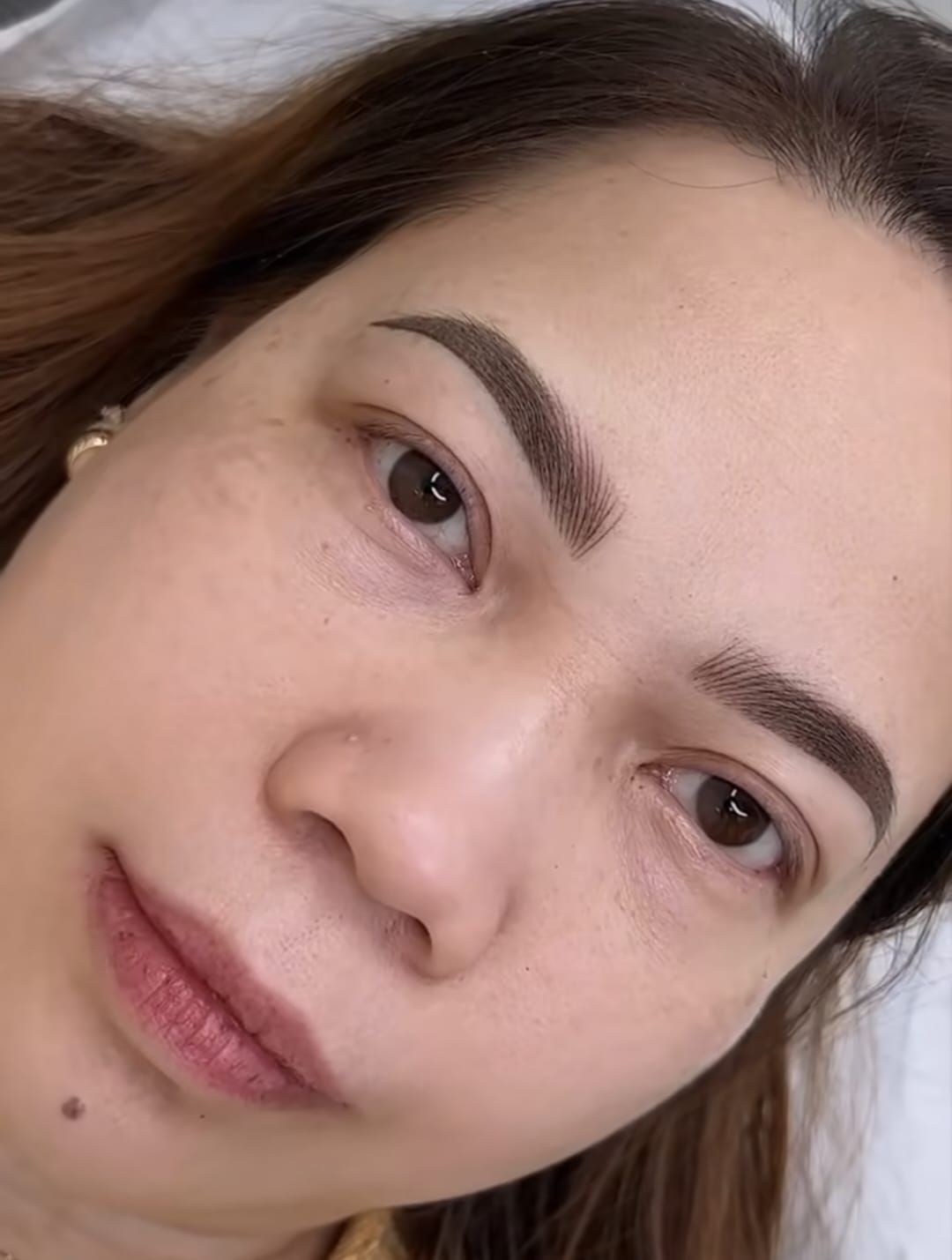Close-up of a person’s face showing recently microbladed, dark brown eyebrows with defined, natural-looking hair strokes.