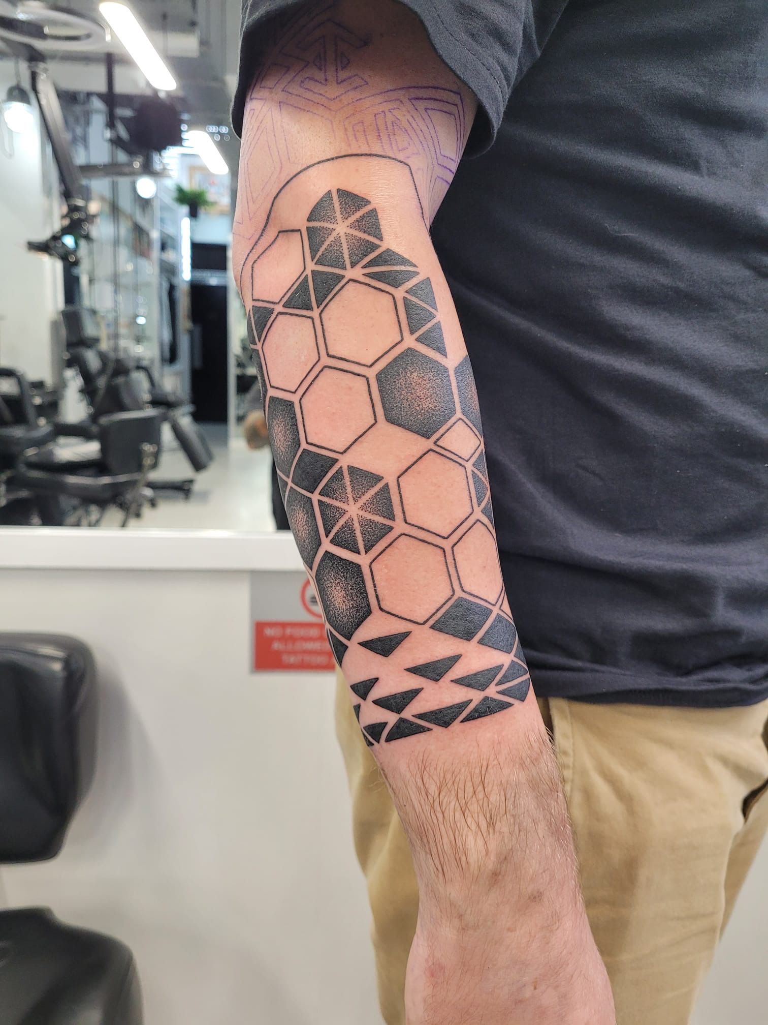 A forearm tattoo featuring a geometric pattern of black-shaded and outlined hexagons fading into triangles at the wrist.