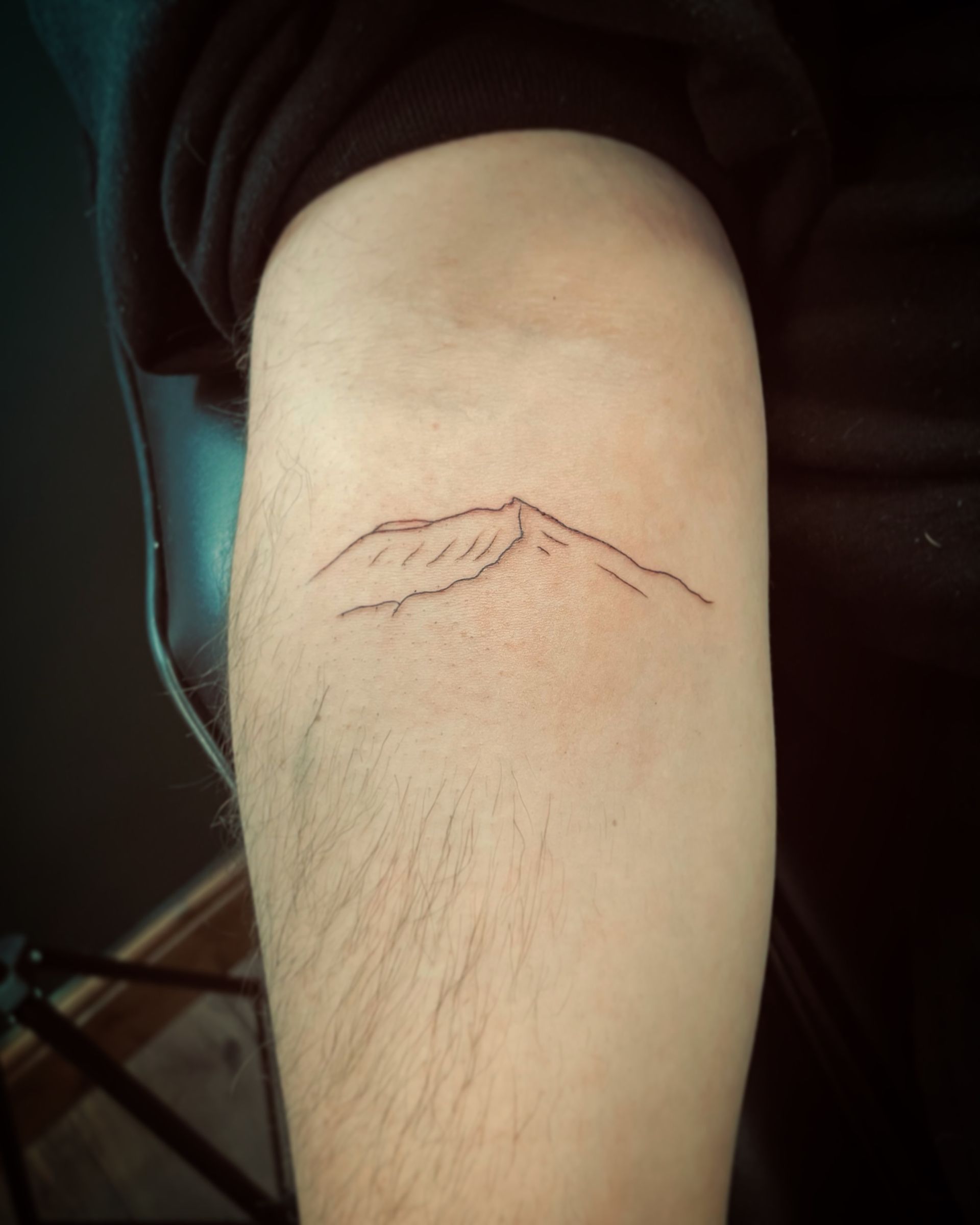 A minimalist, fine-line mountain range tattoo on an arm.