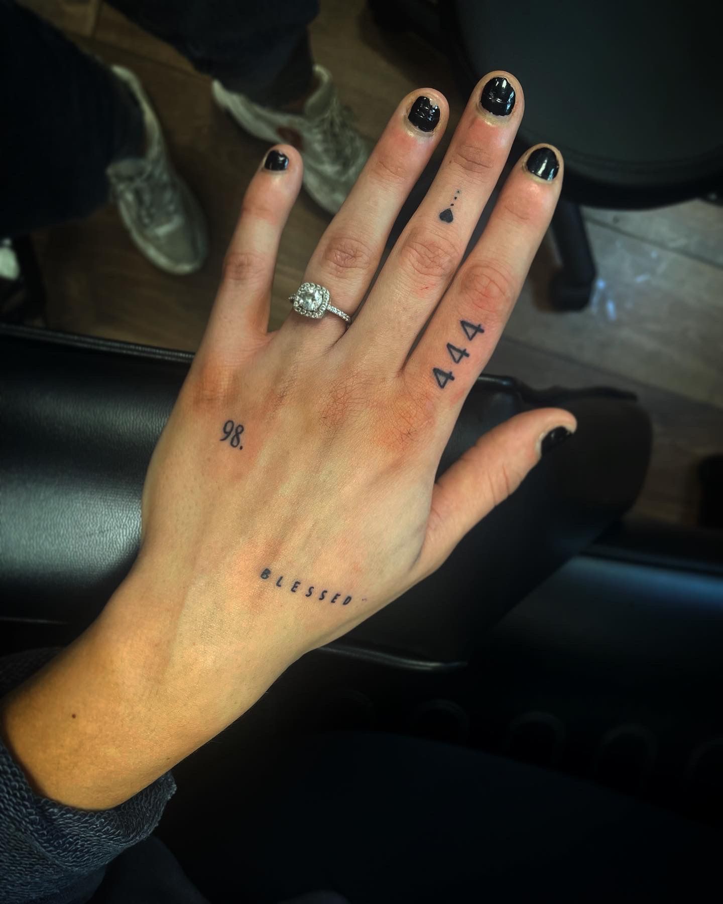 A hand featuring several small, fine-line black ink tattoos, including the numbers 