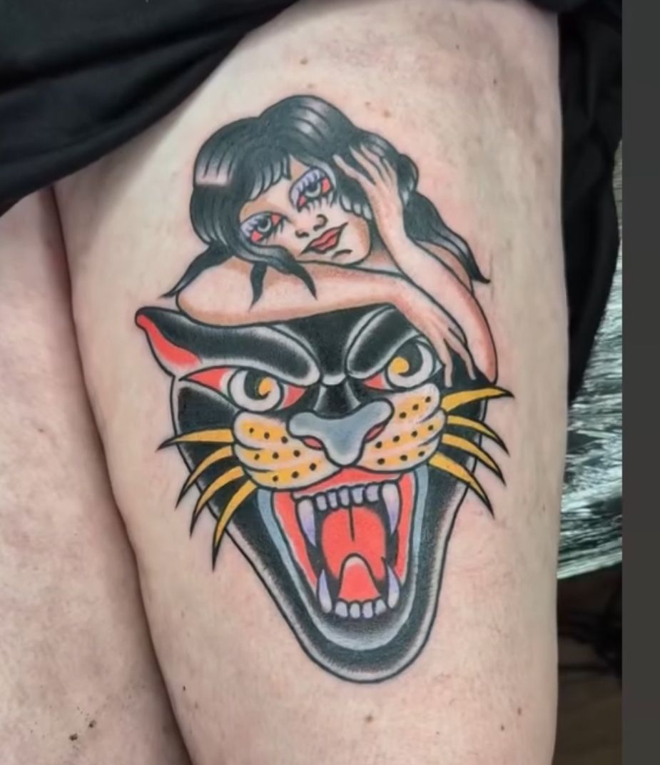 A colorful, traditional-style tattoo of a woman resting her arms on the head of a snarling panther.