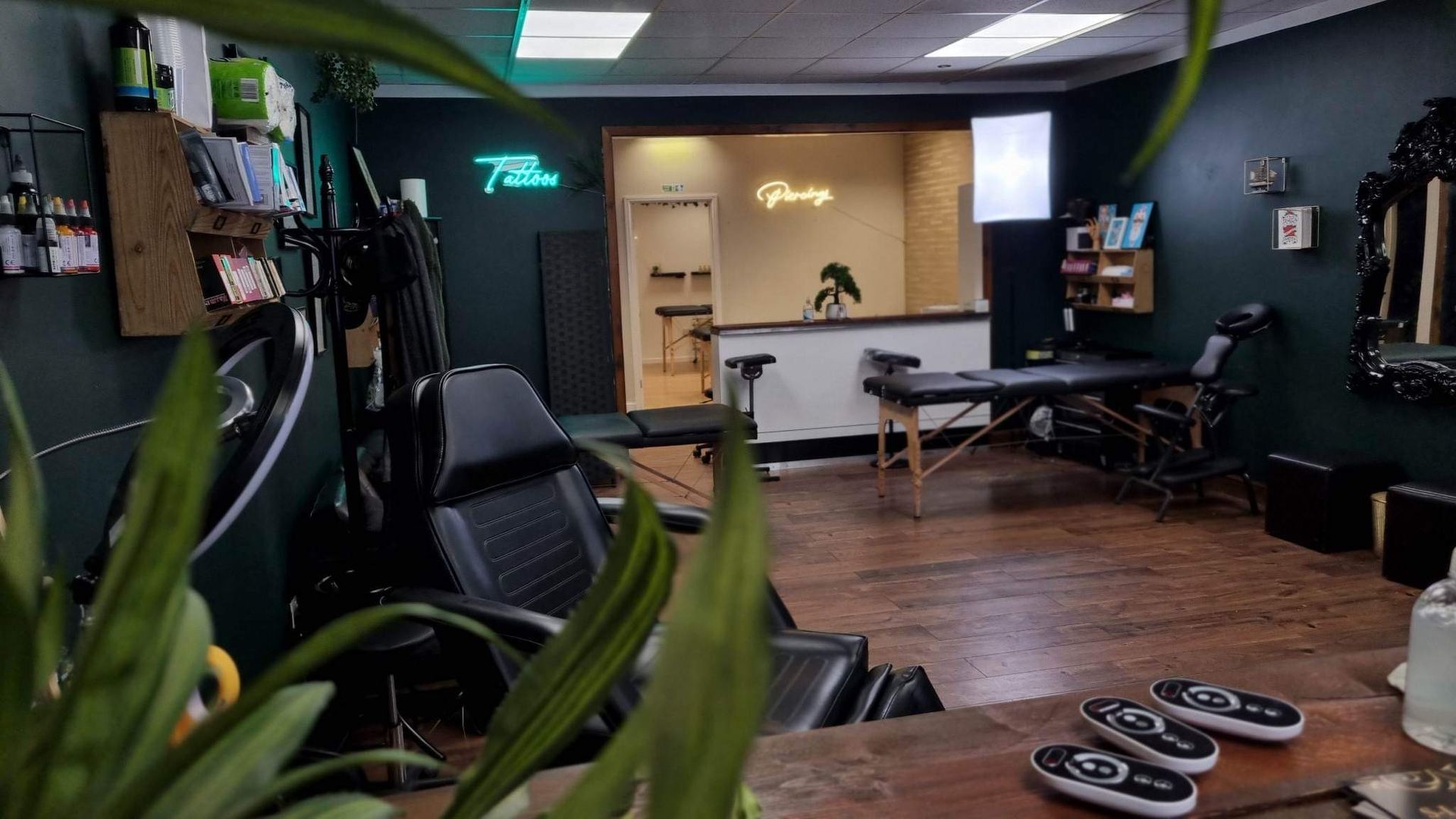 A dimly lit tattoo studio featuring black walls, equipment, a massage table, and wooden floors.