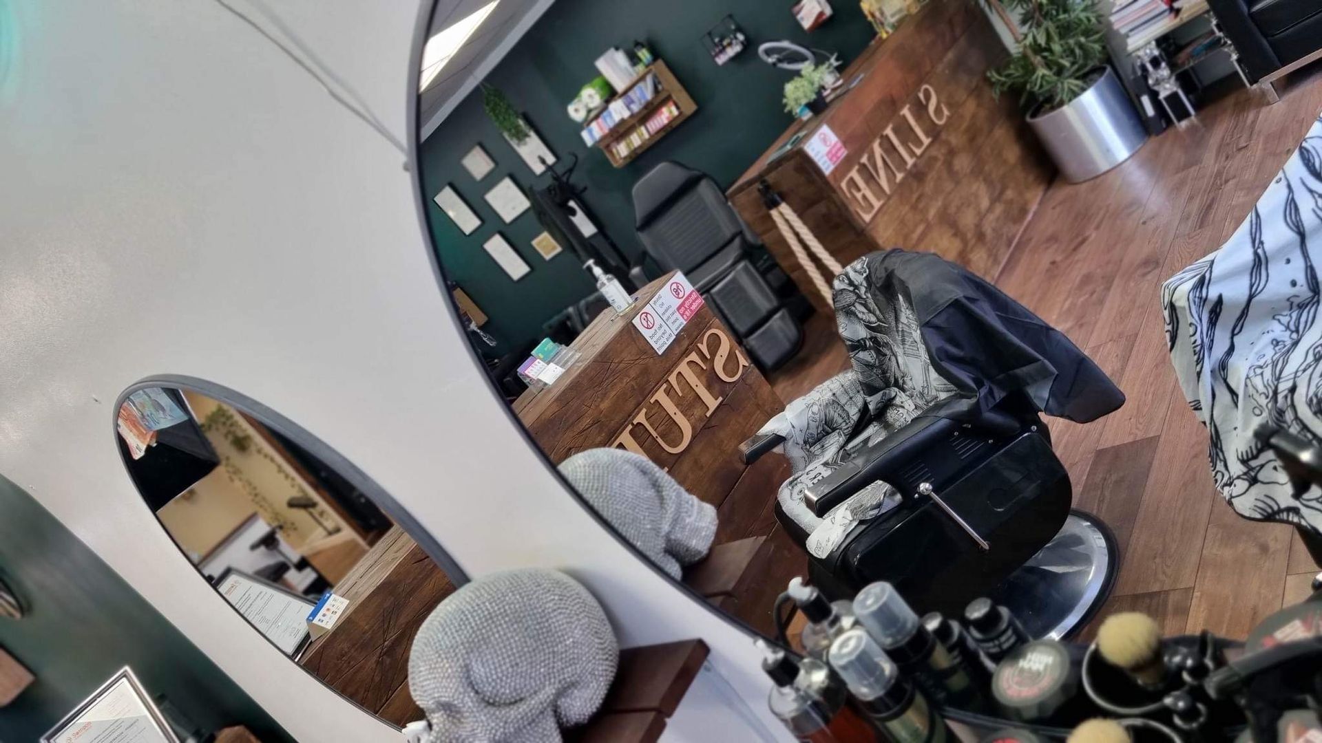 A salon interior features a black styling chair, a wooden desk with 