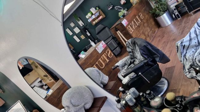 A salon interior features a black styling chair, a wooden desk with 