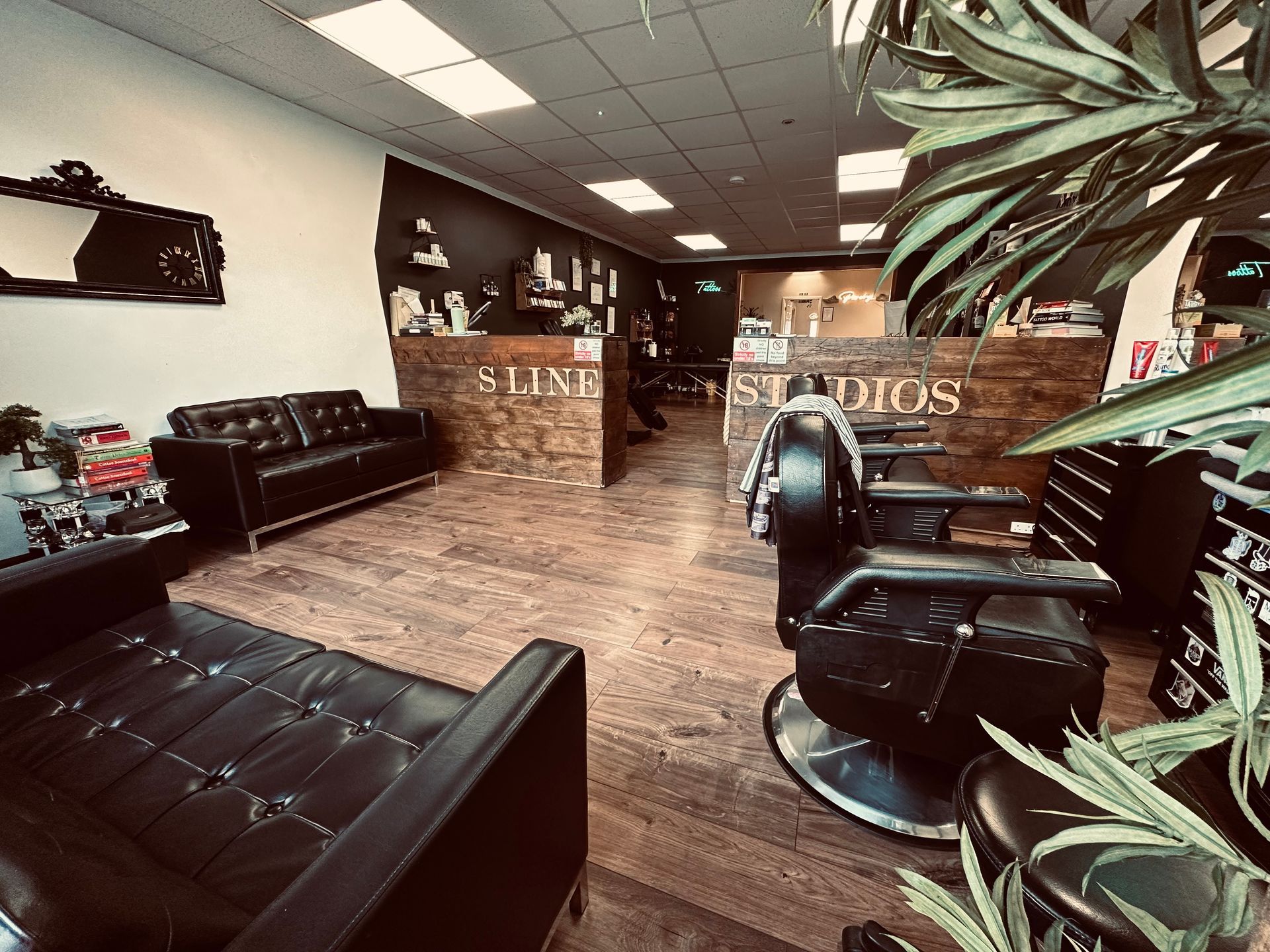 An interior view of a barbershop with black leather chairs, dark wood flooring, and wooden reception desks.