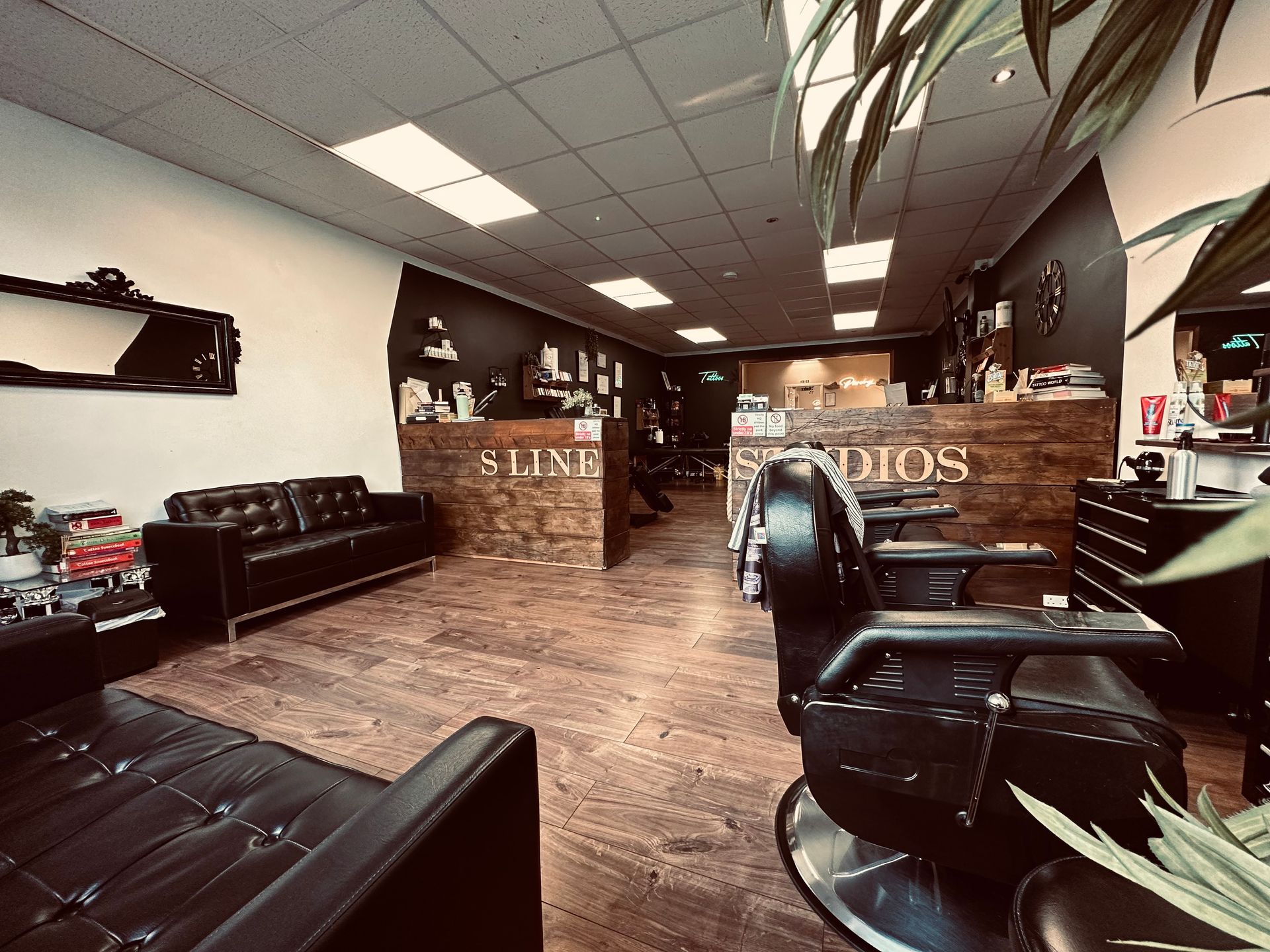 Interior of a modern barbershop with black leather chairs, wood-paneled counters, and hardwood floors.