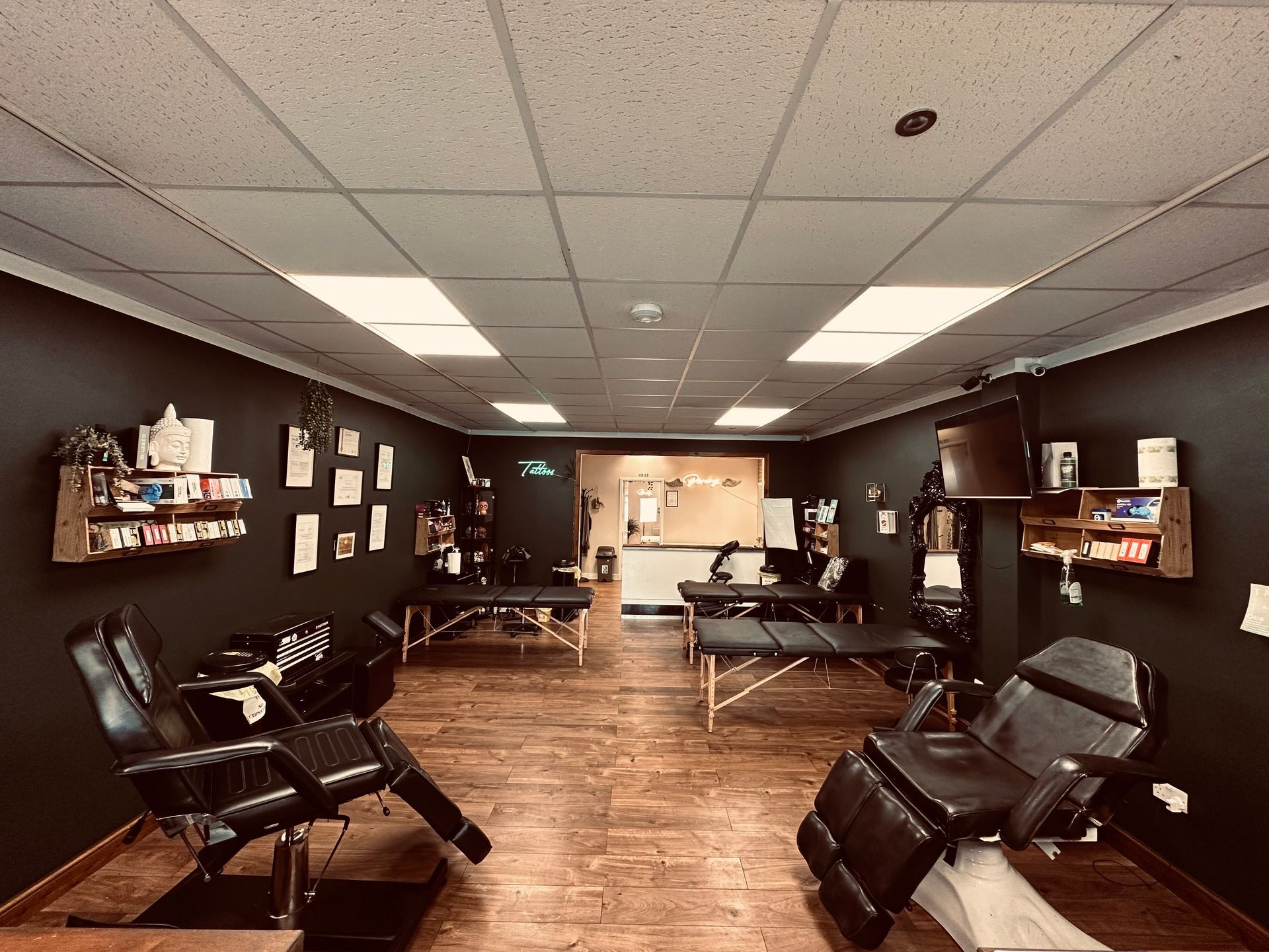 Professional tattoo parlor interior with black walls, wood floors, and multiple tattoo chairs and tables.