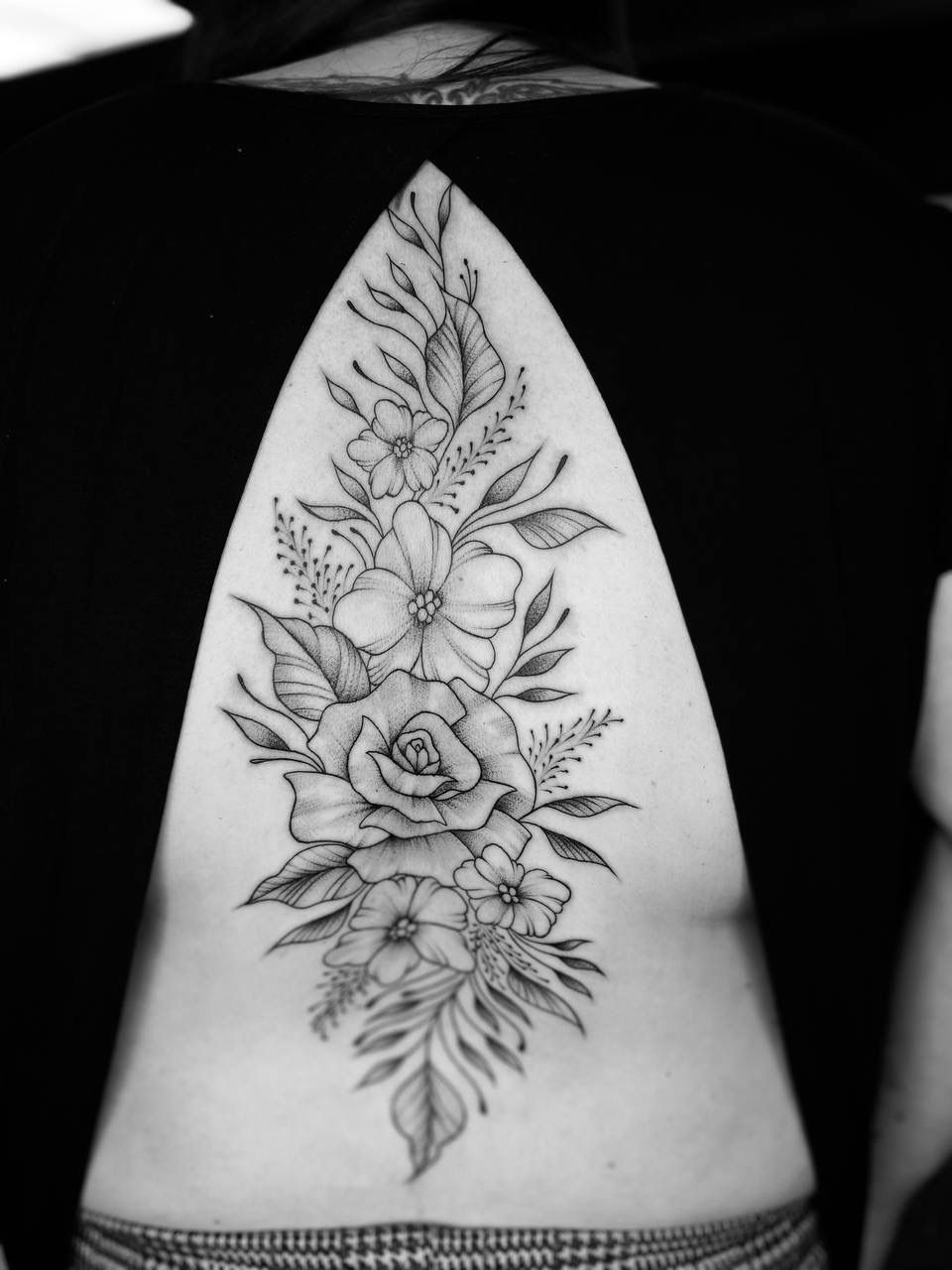 A black and white floral tattoo spanning the center of a person's back, framed by a cutout in their black top.