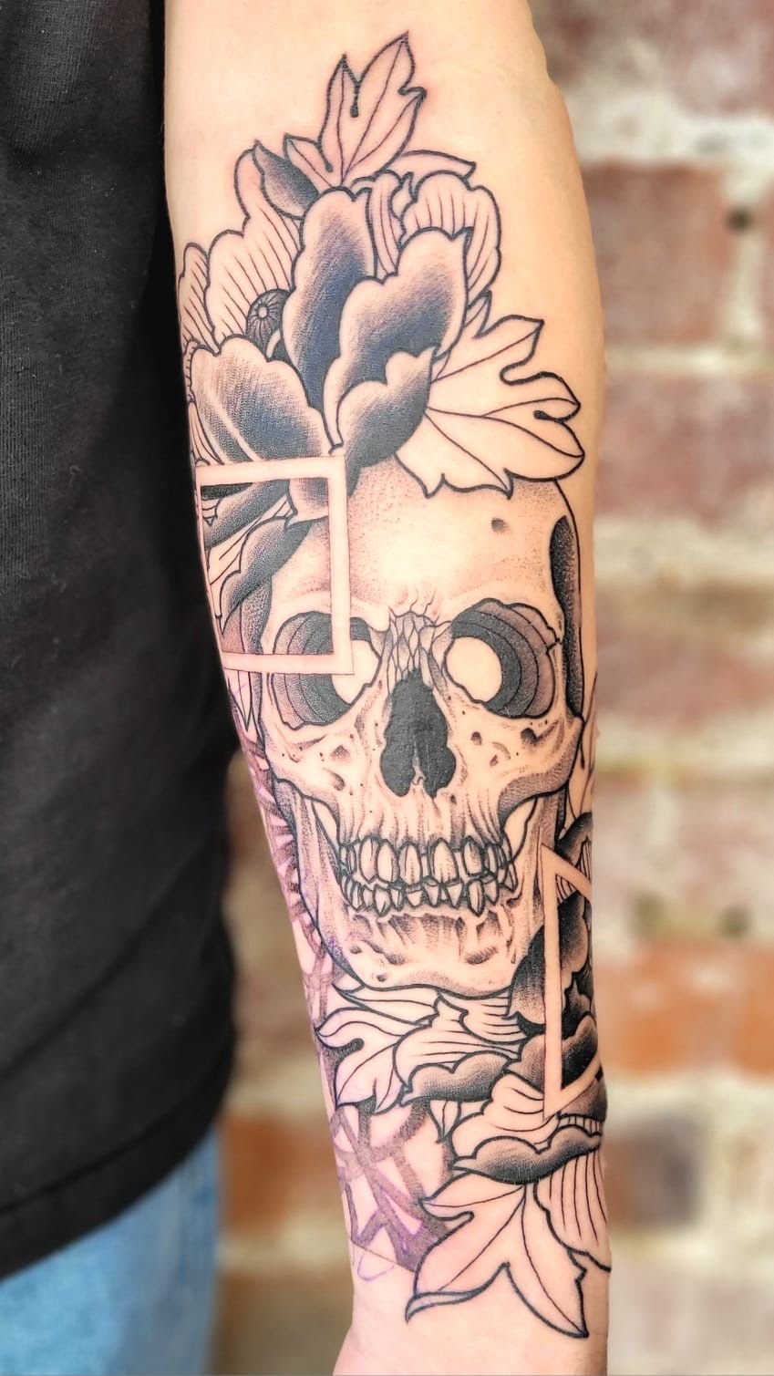 A forearm tattoo featuring a skull surrounded by stylized flower blossoms and thin, geometric square outlines.